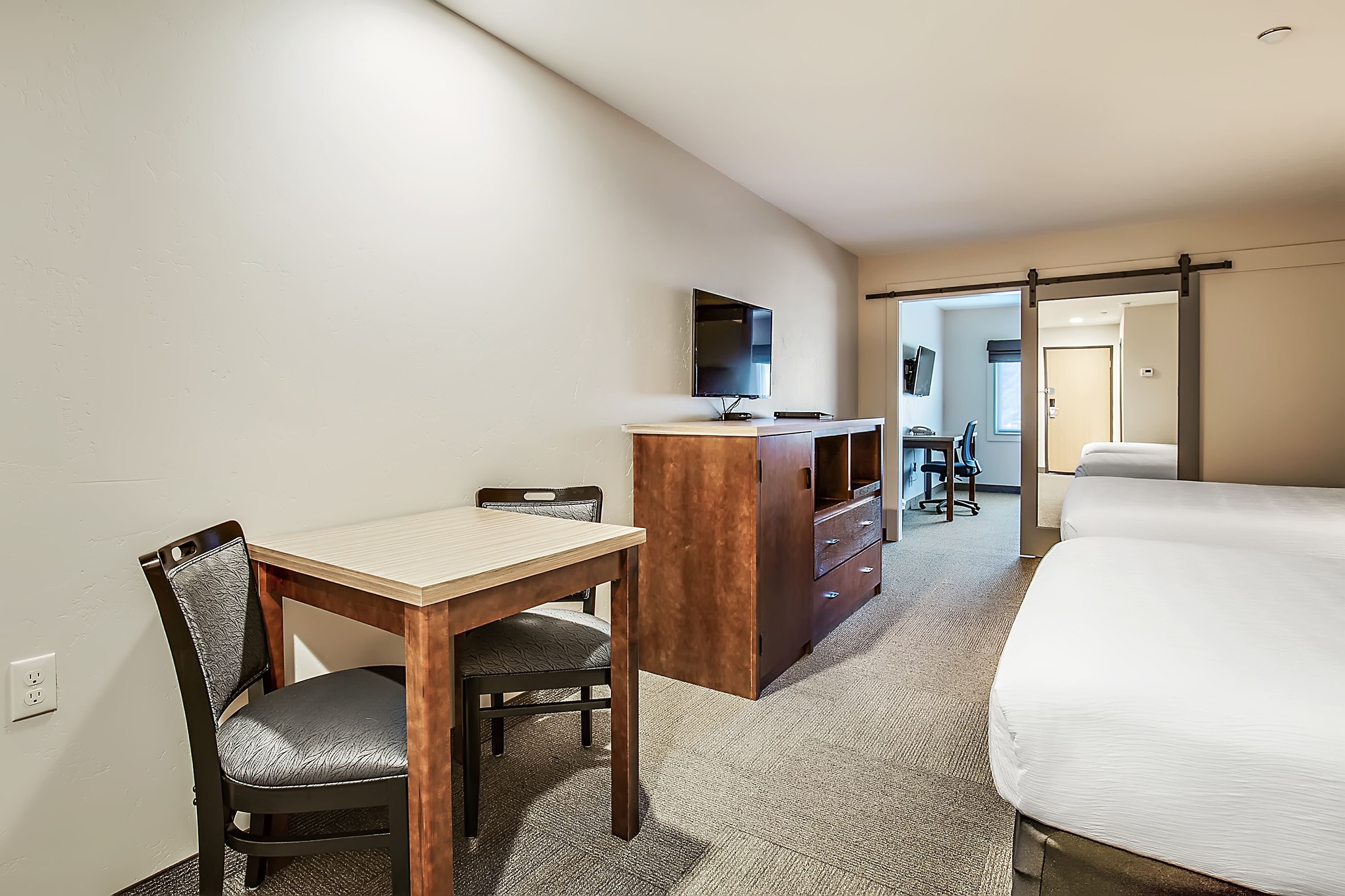 A hotel room with a bed, a desk, a chair, a dresser, and a TV.