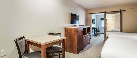 A hotel room with a bed, a desk, a chair, a dresser, and a TV.