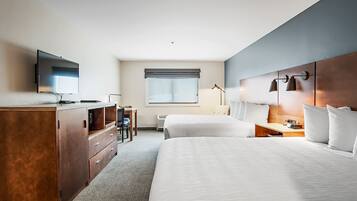 A hotel room with two beds, a desk, a TV, and a window with blinds.