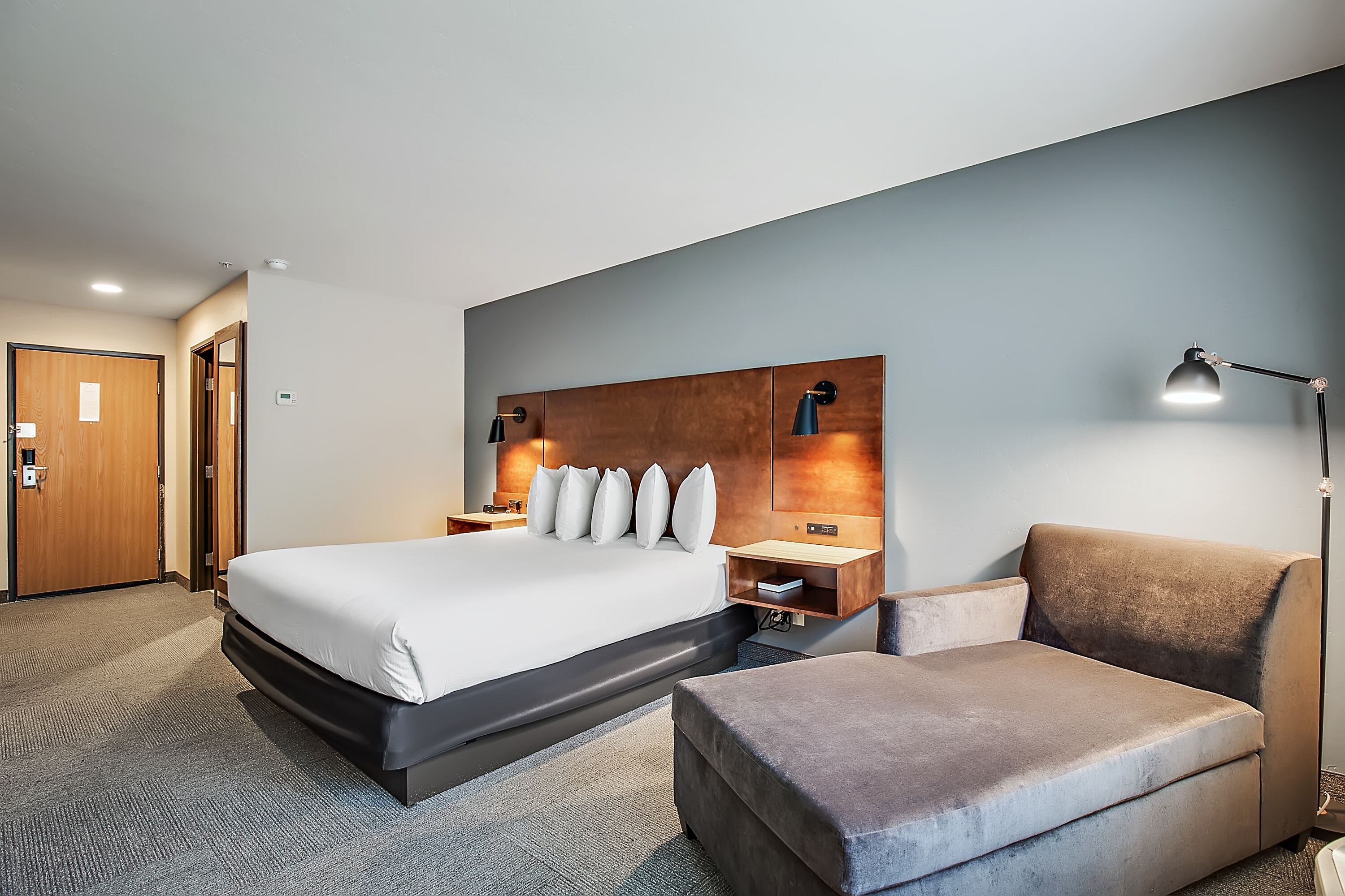 A hotel room with a large bed, a bedside table, a chair, and a desk.