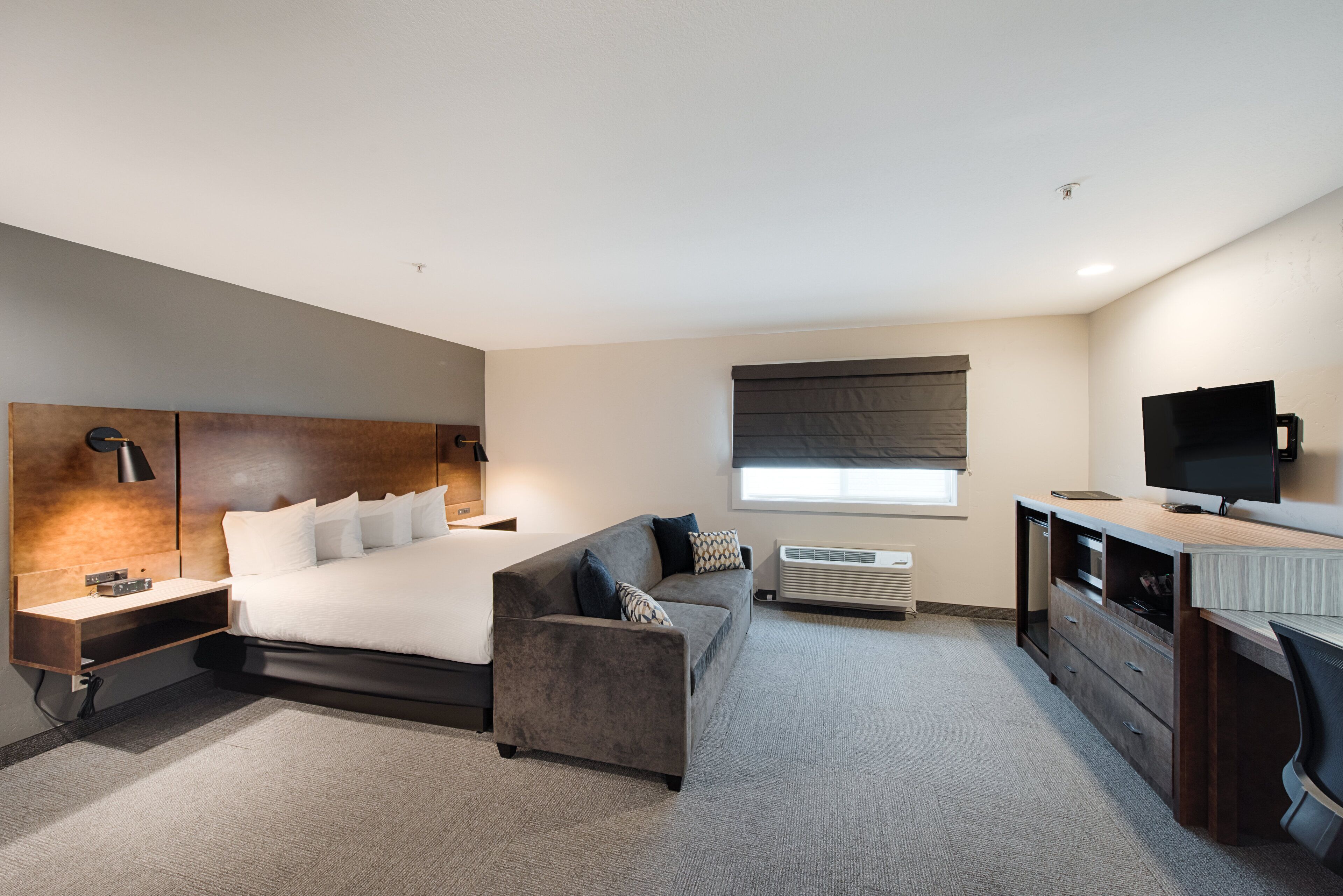 A modern hotel room with a large bed, a sofa, a desk, and a TV.