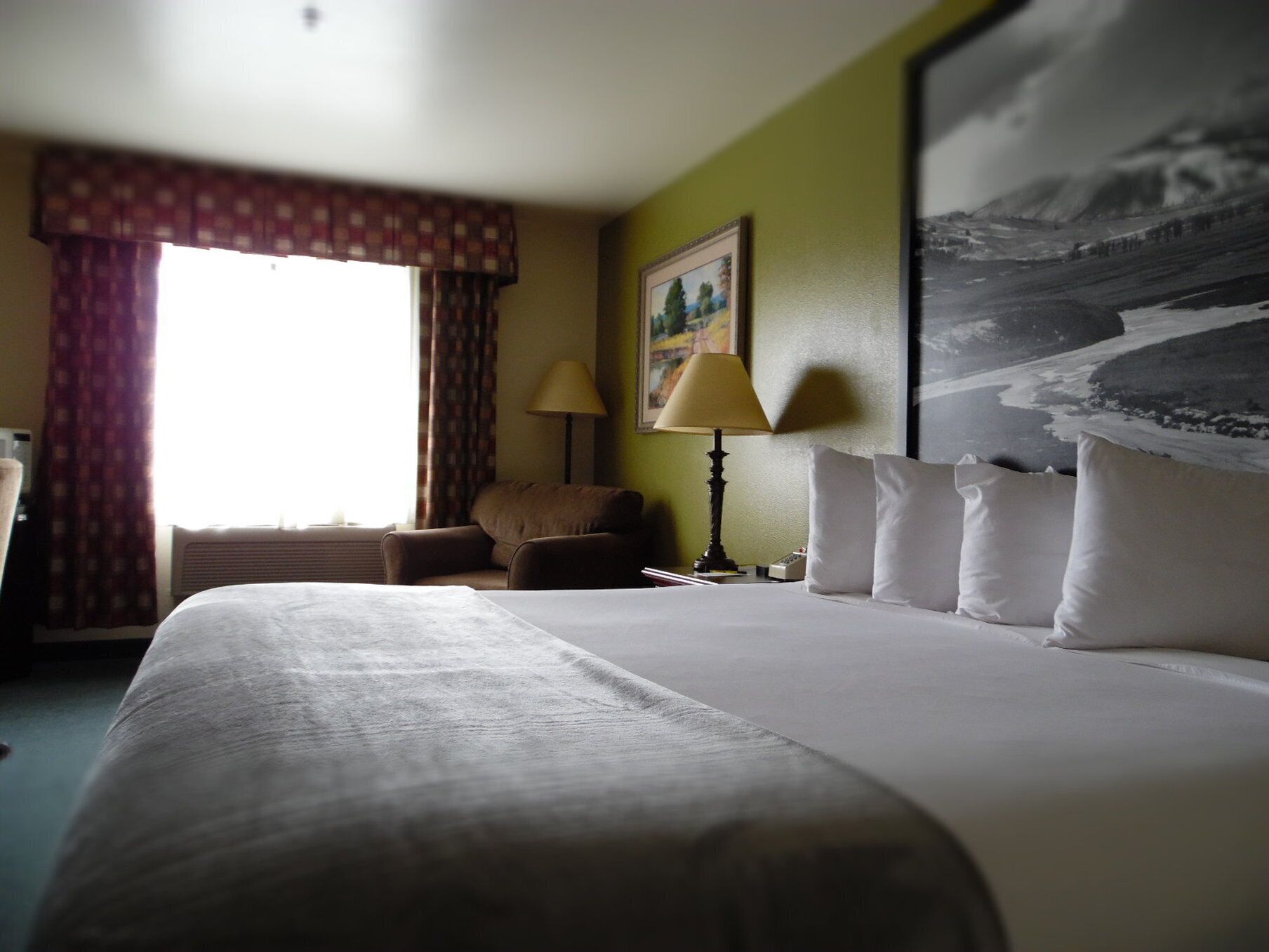 A hotel room with a large bed, a chair, a lamp, and a painting on the wall.