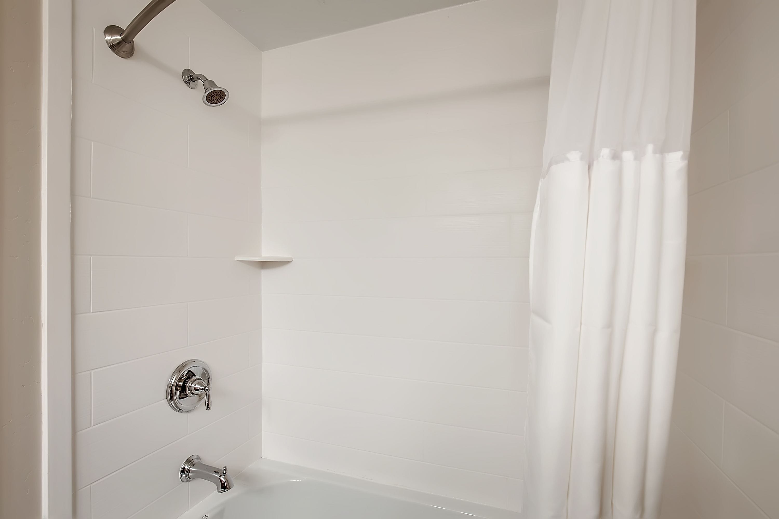 Un baño moderno con azulejos blancos, una bañera, un cabezal de ducha y una cortina.