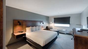 Una habitación de hotel moderna con una cama grande, un escritorio, una silla, una mesita de noche y una ventana con persianas.