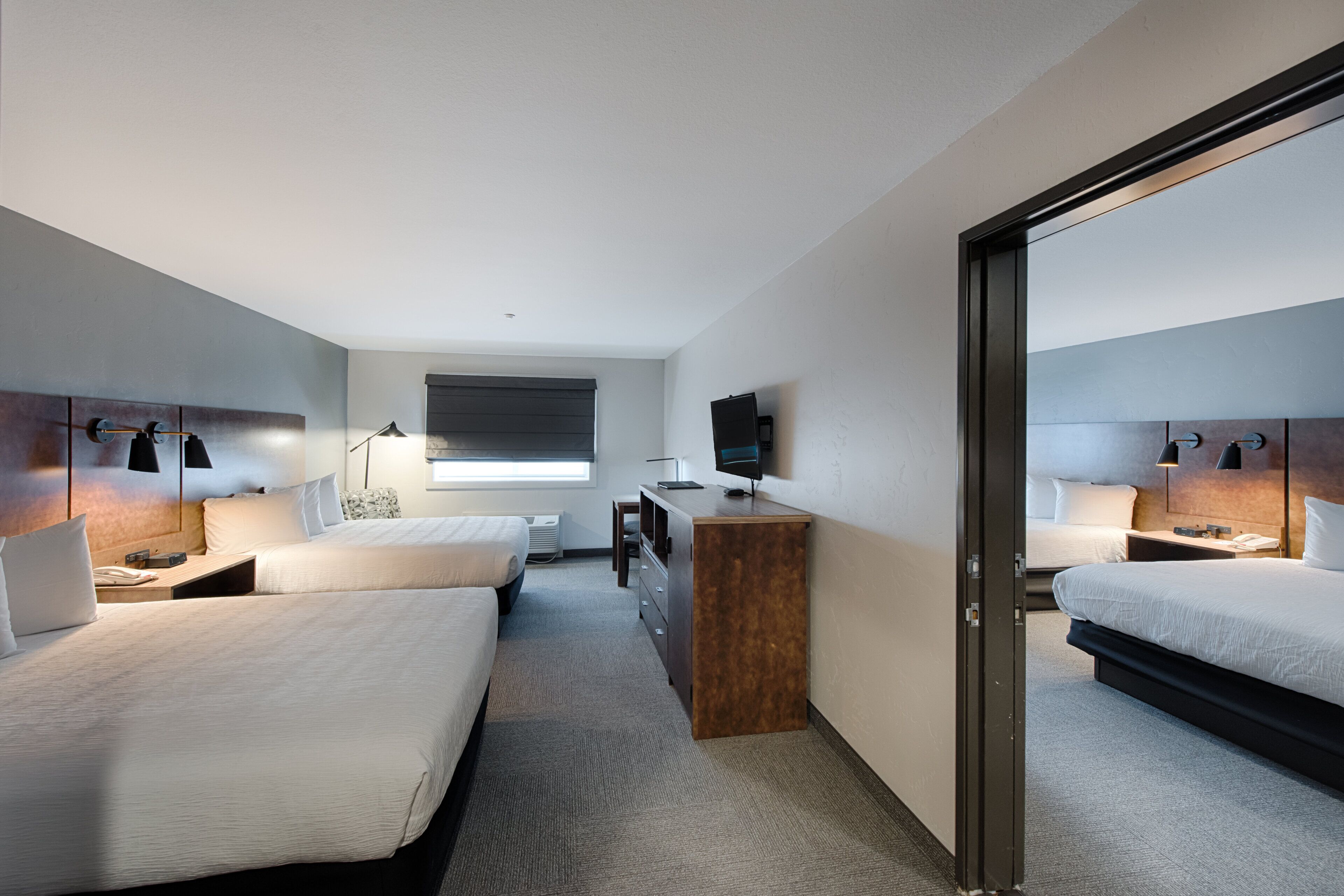 A modern hotel room with two beds, a desk, a chair, a television, and a large mirror.