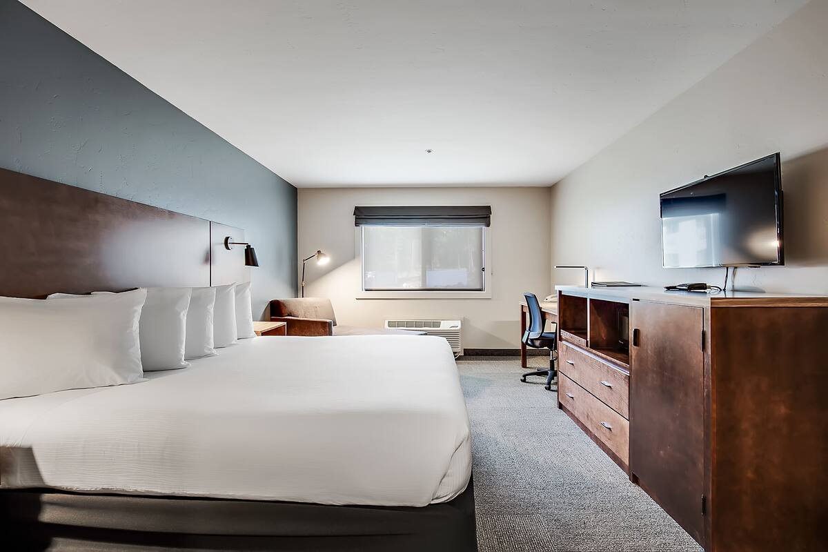 A hotel room with a large bed, a desk, a chair, a TV, and a wardrobe.