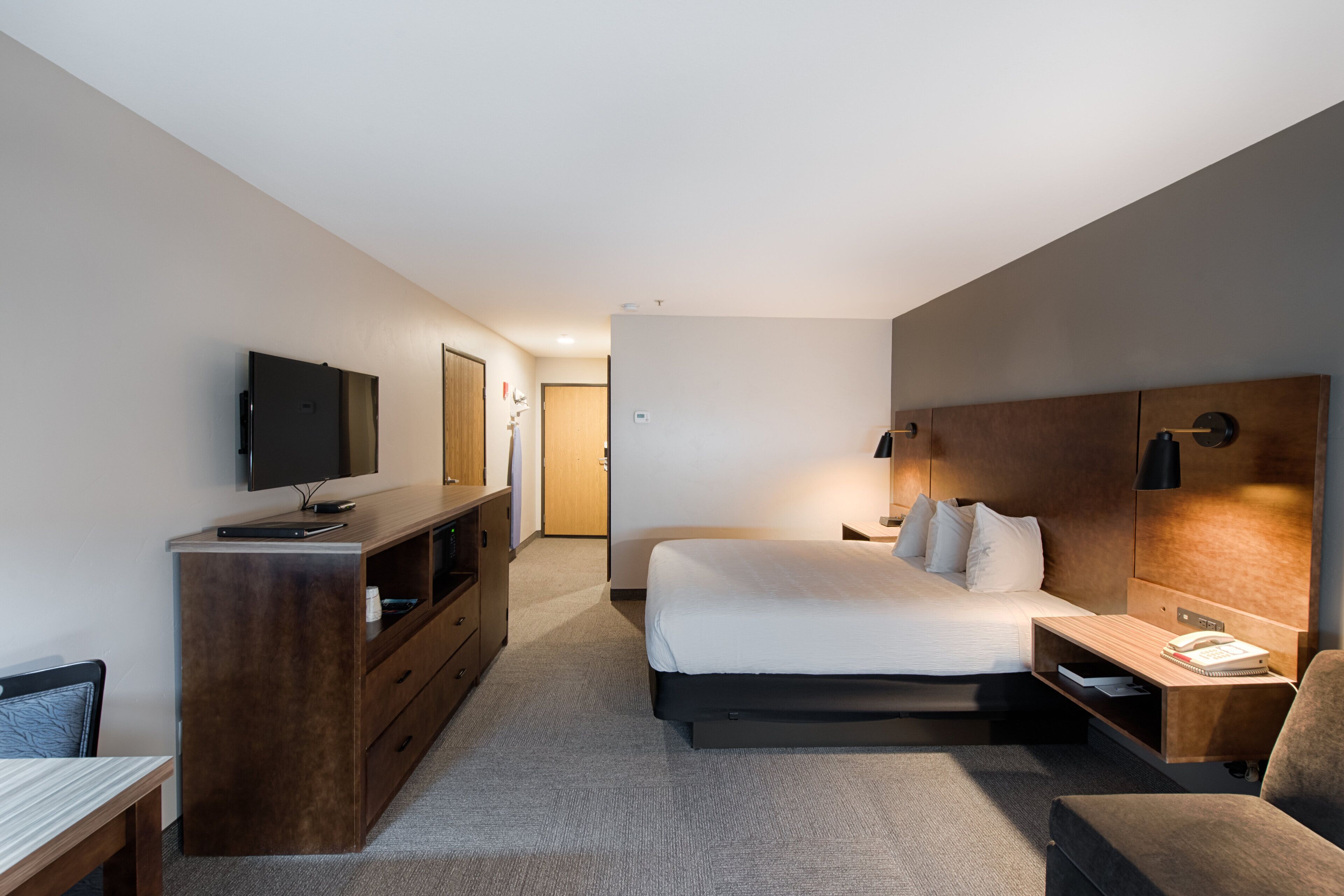 Una habitación de hotel moderna con una cama grande, un escritorio, un televisor y un armario.