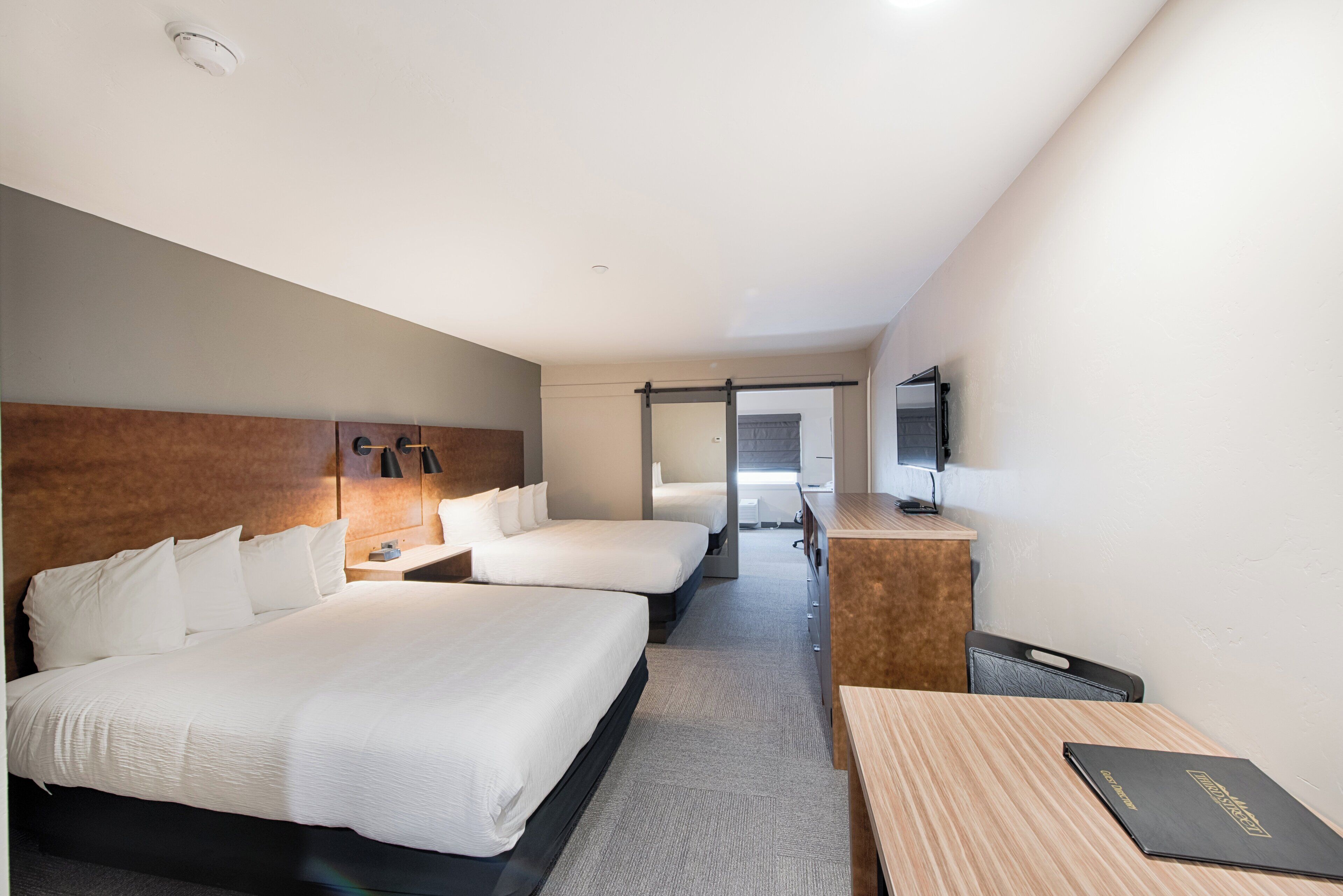 Hotelkamer met twee bedden, een bureau, een stoel, een televisie en een schuifdeur naar een andere kamer.