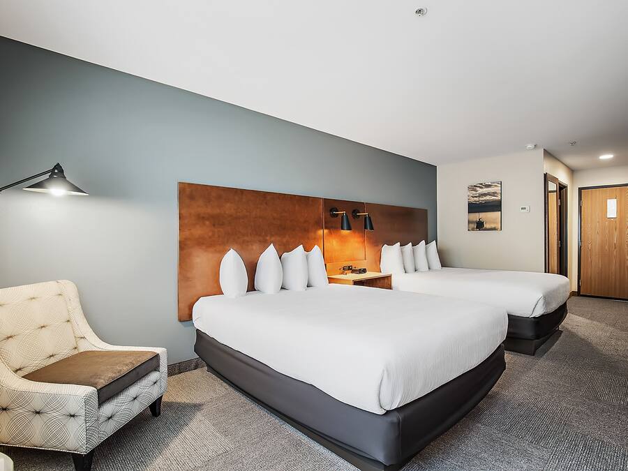 Una habitación de hotel con una cama grande, una mesita de noche, una lámpara y una silla.