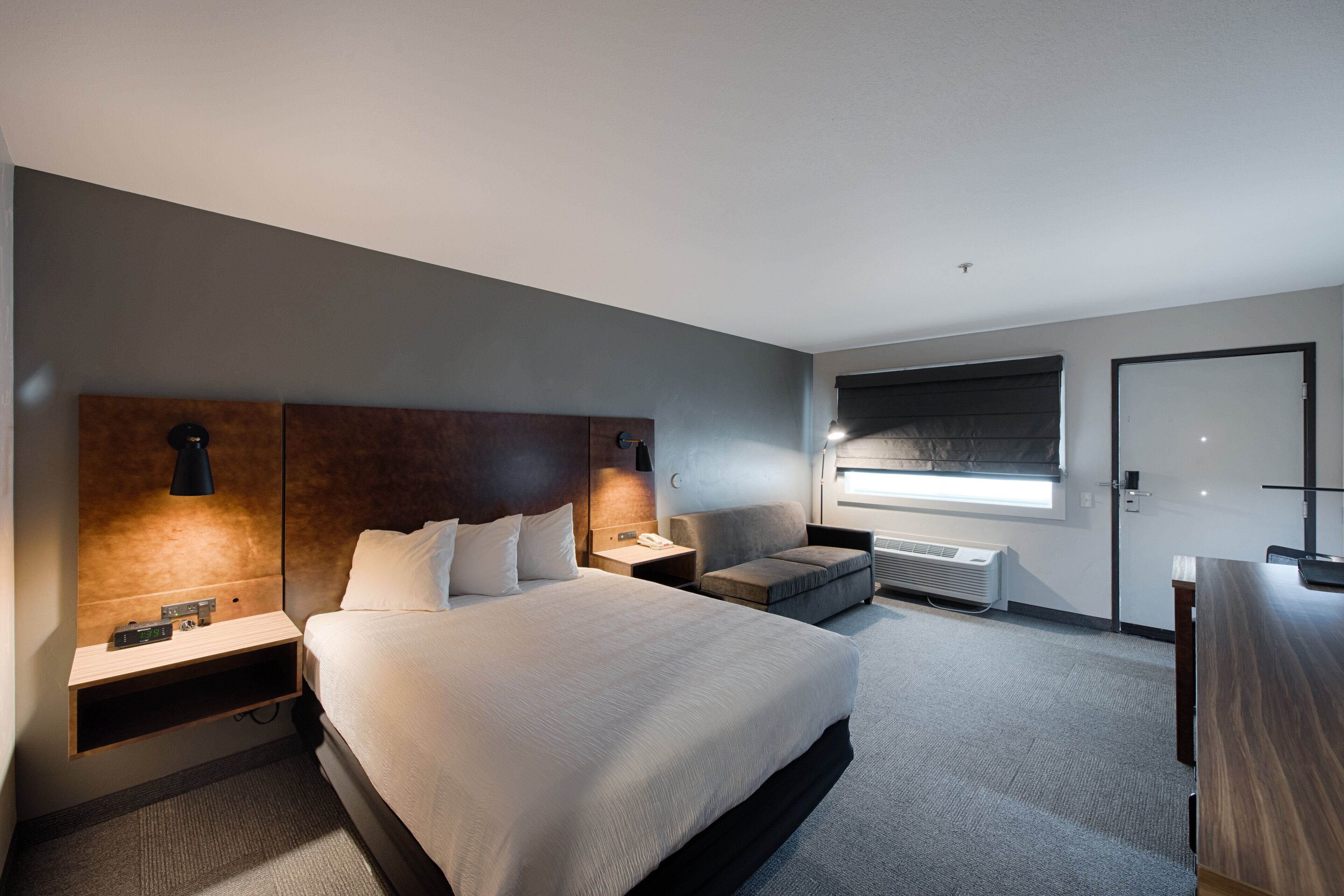 Una habitación de hotel moderna con una cama grande, mesitas de noche, un escritorio y una ventana con persianas.