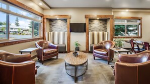A spacious lobby with leather chairs, a round wooden table, and large windows offering a view of the outside. - Third Street Inn (McCall)
