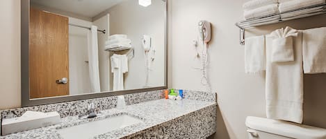 Une salle de bain dotée d’un lavabo avec un plan de travail en granit, d’un grand miroir, d’un sèche-cheveux et d’un porte-serviettes avec des serviettes pliées.