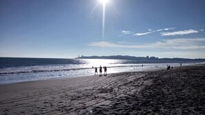 Una platja amb empremtes que condueixen a l'aigua, un cel clar i edificis lluny.