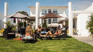 Zona de piscina amb gandules i ombrel·les, envoltada d'edificis blancs i vegetació.