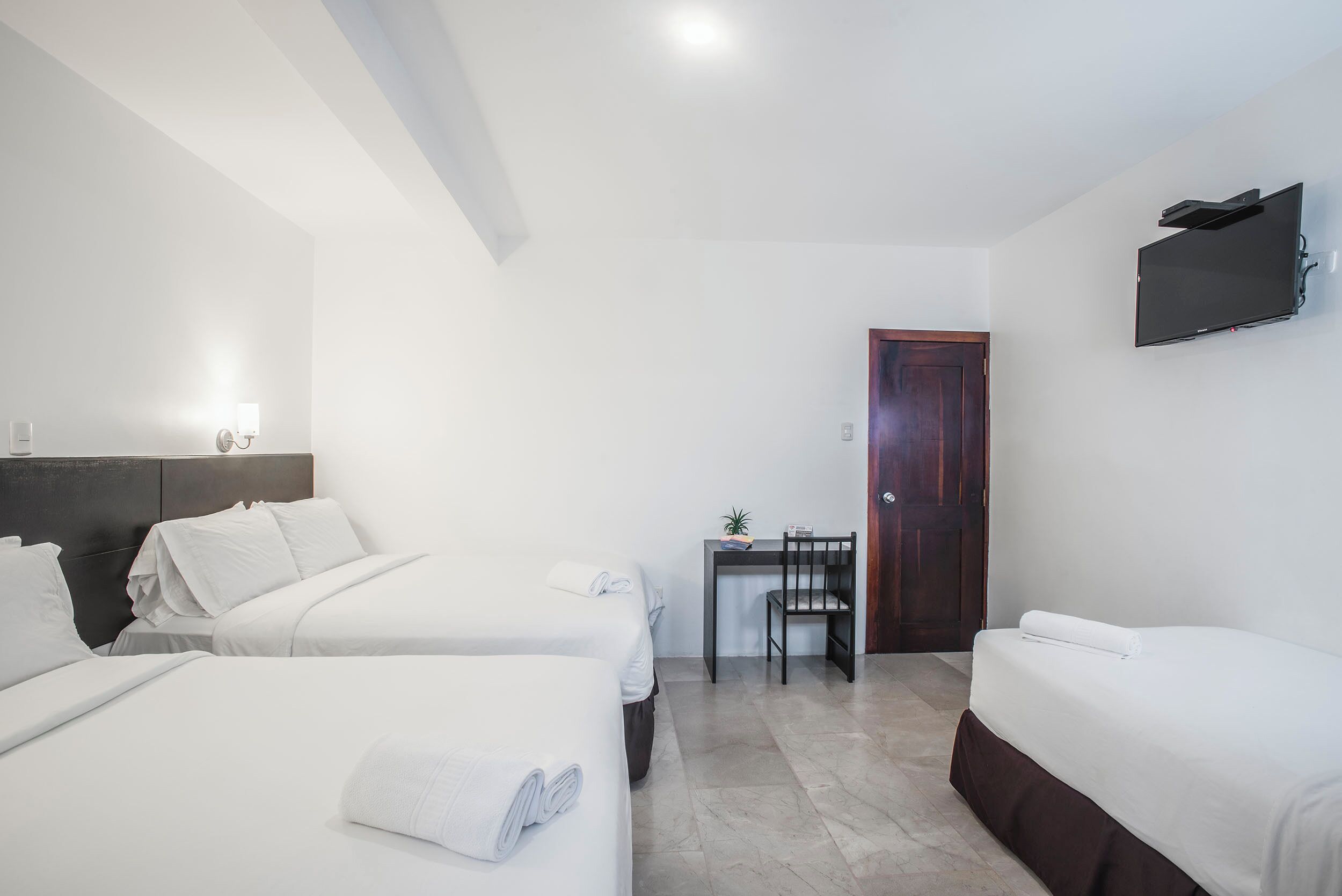 Habitación de hotel con dos camas, un escritorio, una silla, un televisor y una puerta.