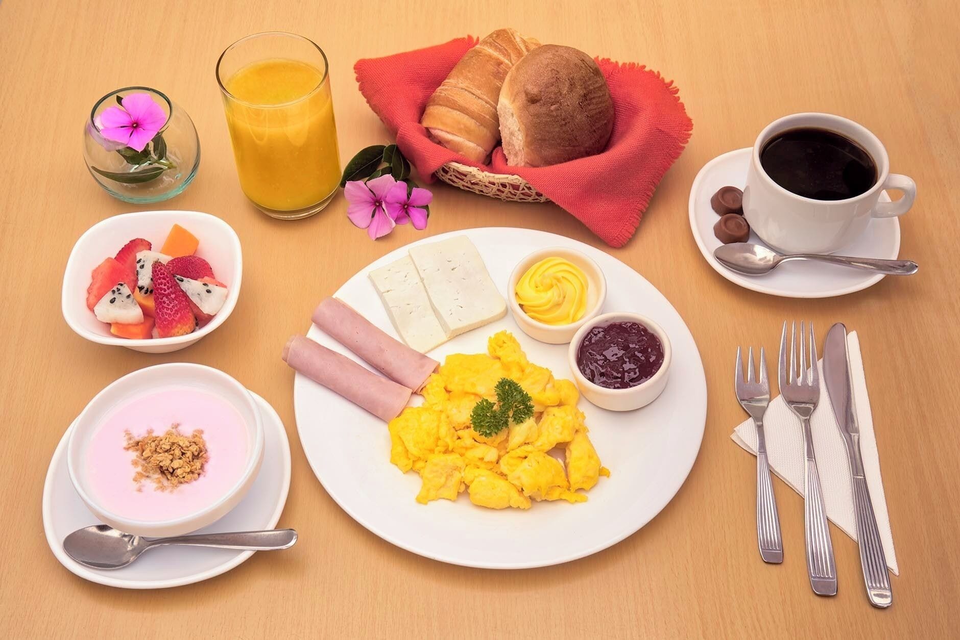 Desayuno con huevos revueltos, jamón, queso, tostadas, fruta, yogur y café.