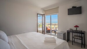 Un dormitori amb un llit gran, un escriptori amb cadira, una televisió i vista a la platja.