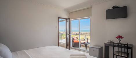 Un dormitorio con una cama grande, un escritorio con una silla, un televisor y vista a la playa.