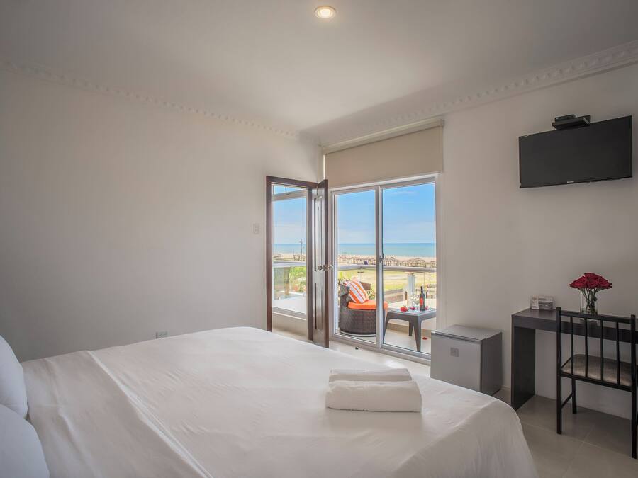 Un dormitorio con una cama grande, un escritorio con una silla, un televisor y vista a la playa.