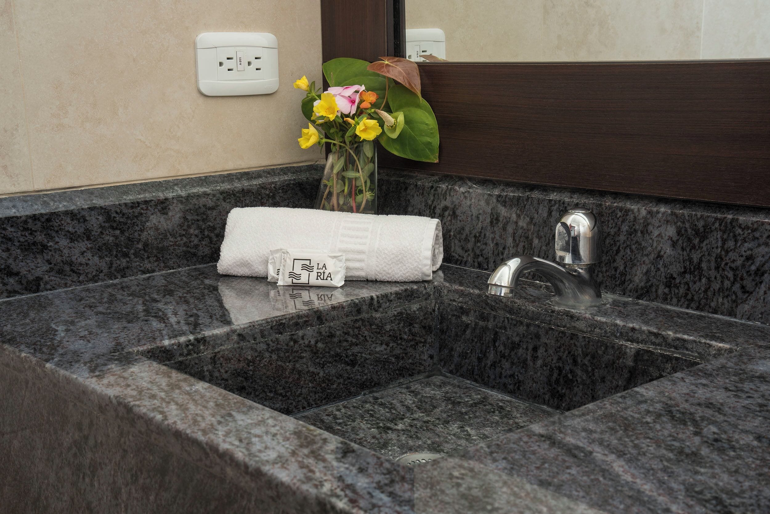 A bathroom with a granite sink, a towel, and a vase with flowers.
