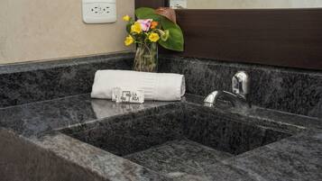 A bathroom with a granite sink, a towel, and a vase with flowers.