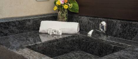 A bathroom with a granite sink, a towel, and a vase with flowers.