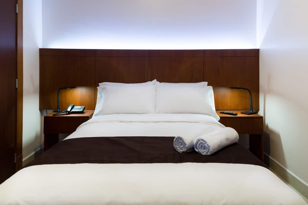 A neatly made bed with white and brown bedding, two bedside tables with lamps, and a wooden headboard.