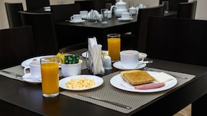 A breakfast setting with a table set for two, including plates of scrambled eggs, toast, and ham, a glass of orange juice, and a teapot.