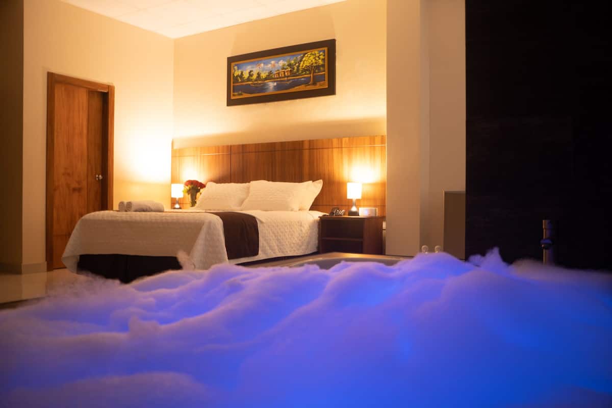 A hotel room with a bed, bedside lamps, a painting on the wall, and a wooden door.
