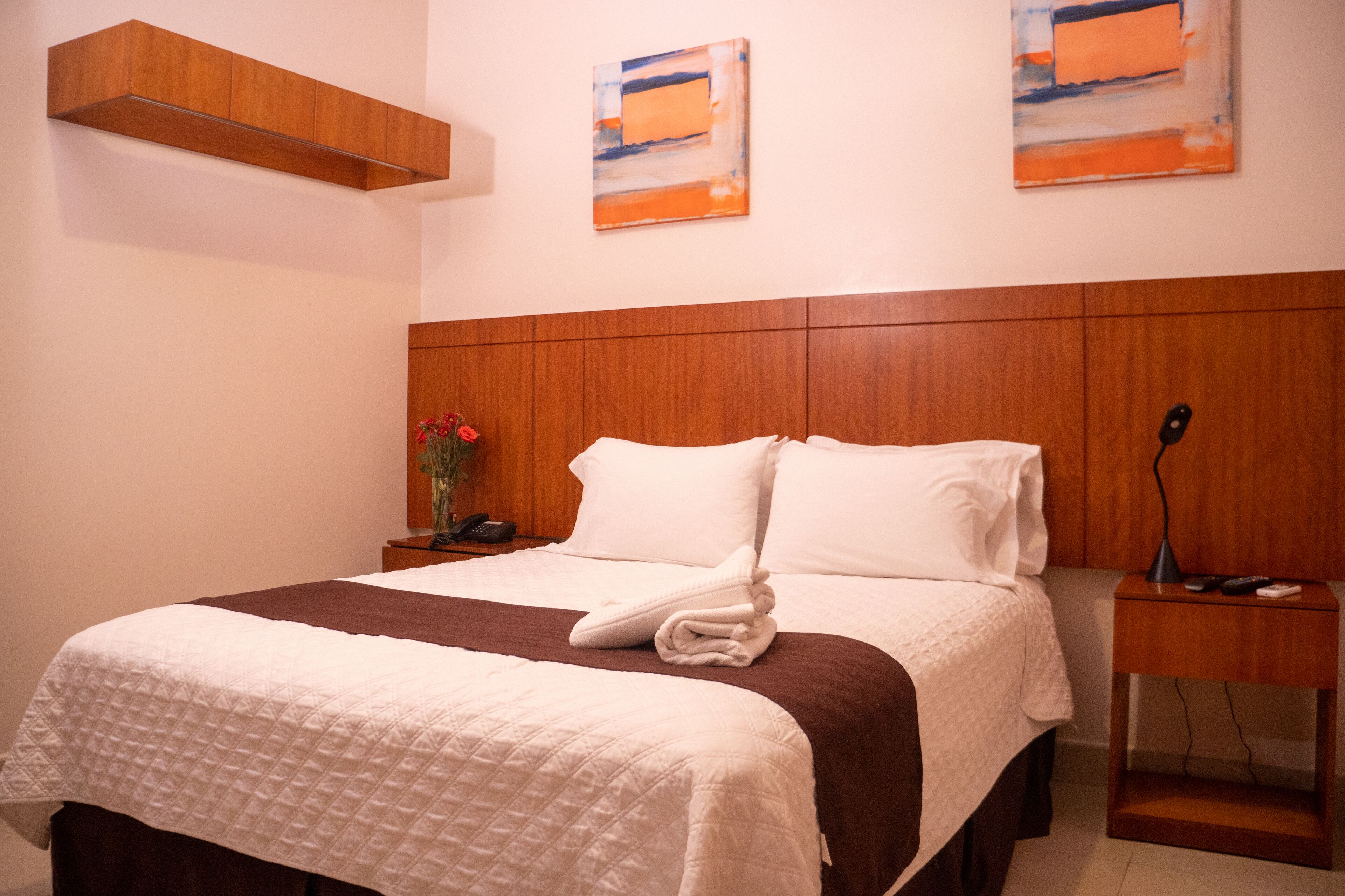 Una cama bien tendida con un edredón marrón y blanco, un cabecero de madera y dos cuadros abstractos en la pared.