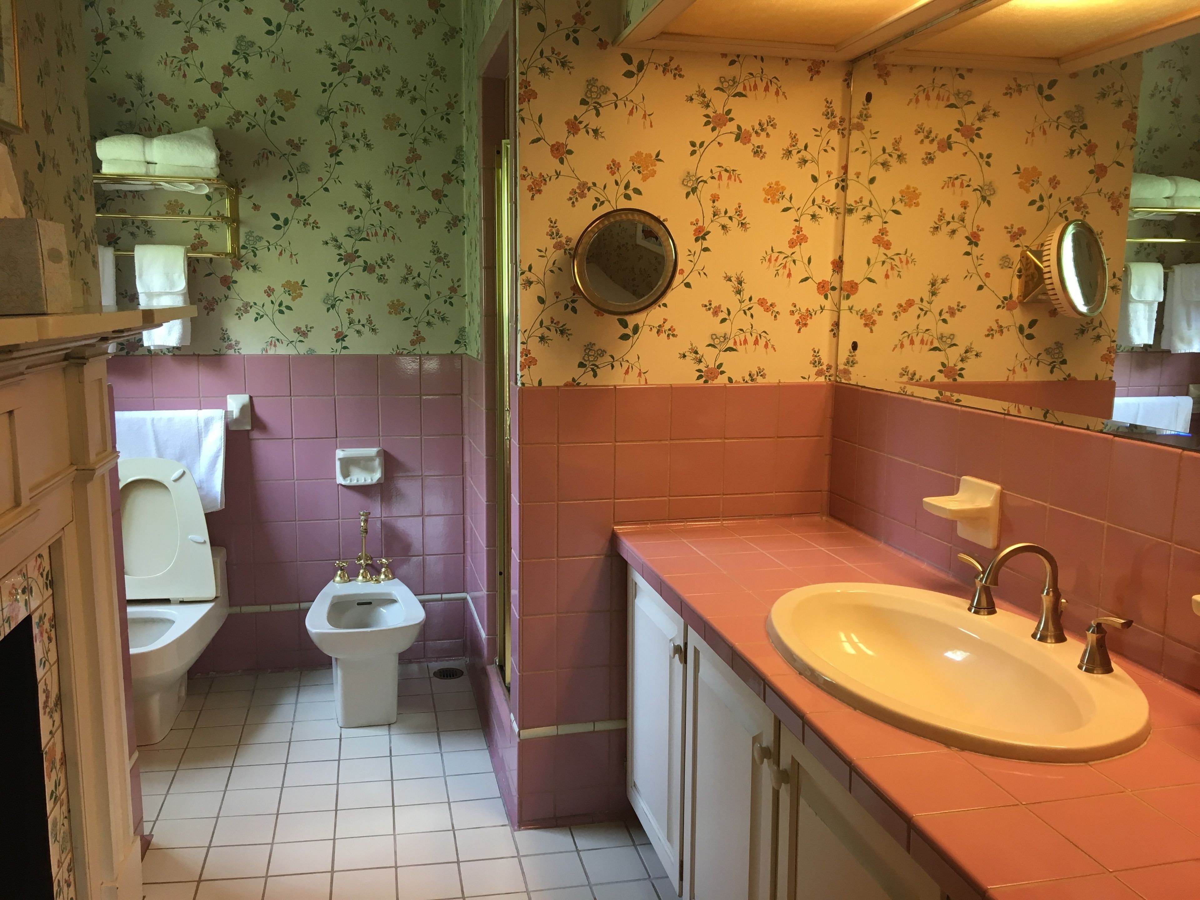 A bathroom with a toilet, bidet, sink, and two mirrors.