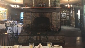 Una chimenea de piedra con repisa, rodeada de mesas y sillas de comedor.
