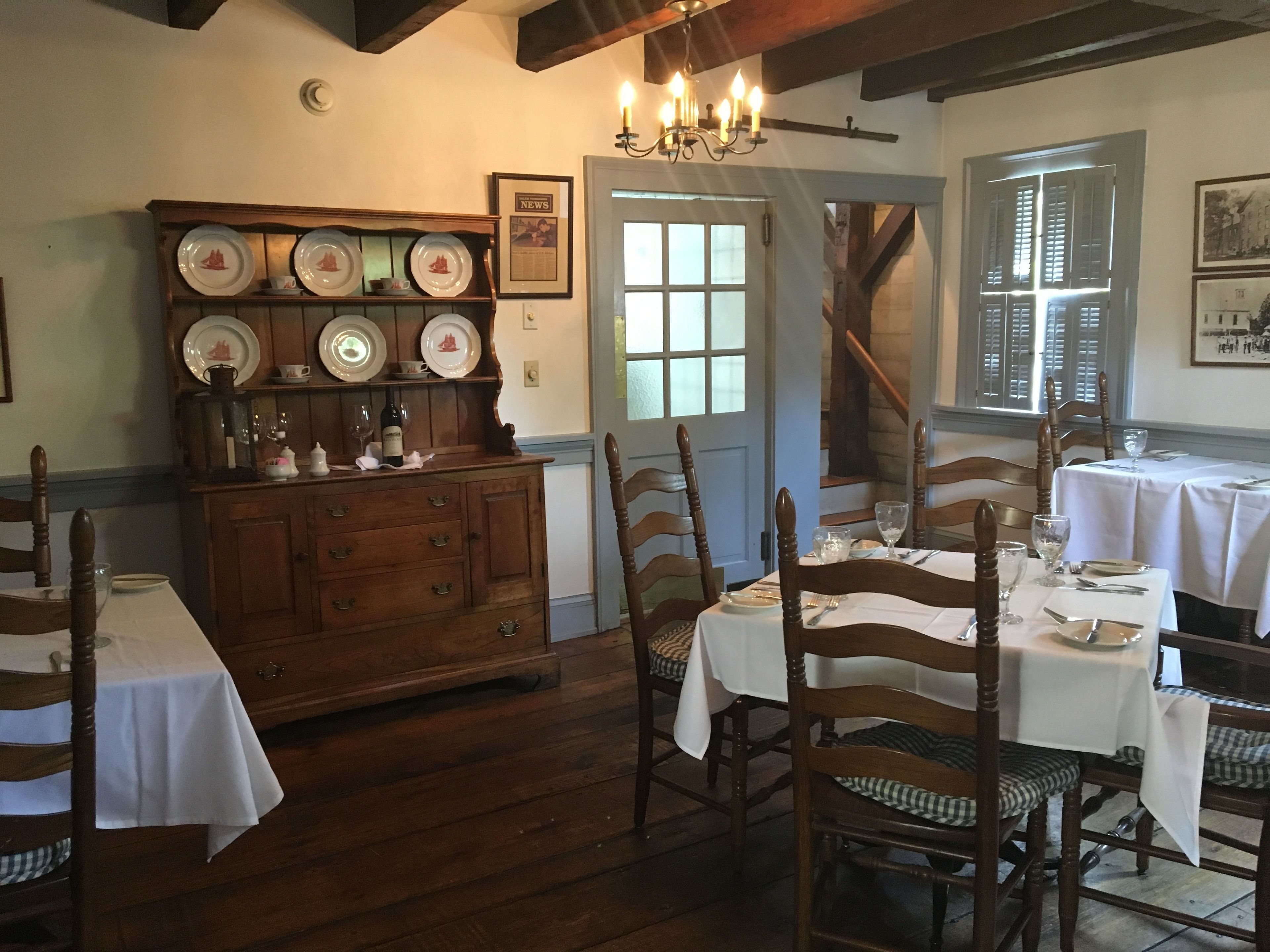 A dining room with wooden tables and chairs, a wooden buffet with plates, and a chandelier.