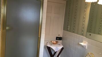 Een badkamer met een witte wastafel, een gouden kraan en een spiegel erboven. Er staat een klein tafeltje met een mand en glazen, en een deur met een gouden omlijsting.