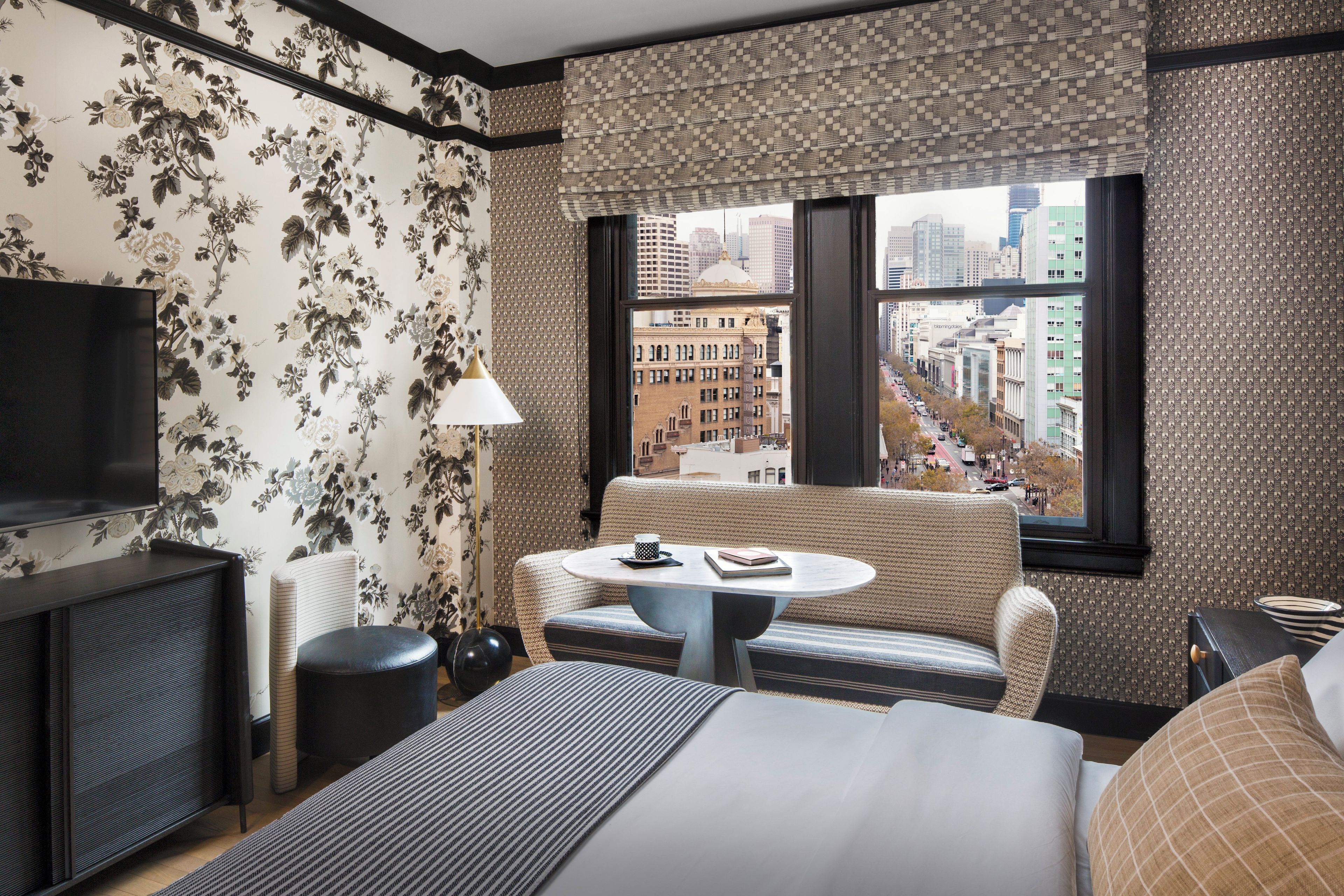 A hotel room with a bed, a round table, a sofa, a TV, and a window with a city view.