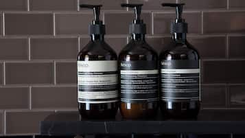 Three bottles of Aesop products on a black surface against a tiled wall.