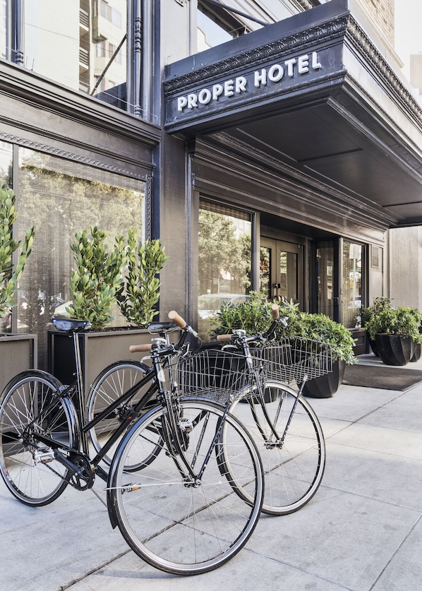 A hotel entrance with a sign reading "PROPER HOTEL," bicycles parked in front, and potted plants.