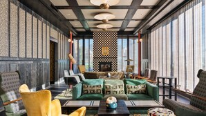 Un interior moderno con una pared a cuadros, sofás verdes con cojines estampados y una mesa central con un jarrón decorativo.