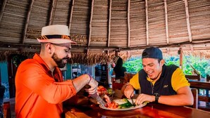 Dos personas cenando en una mesa de madera bajo un techo de paja.