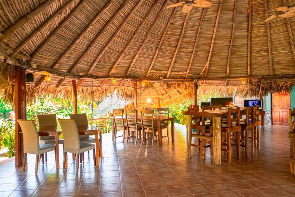 A spacious outdoor dining area with thatched roof, wooden tables, and chairs.