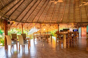 A spacious outdoor dining area with thatched roof, wooden tables, and chairs. - La Pintada Inn (Llano Grande)