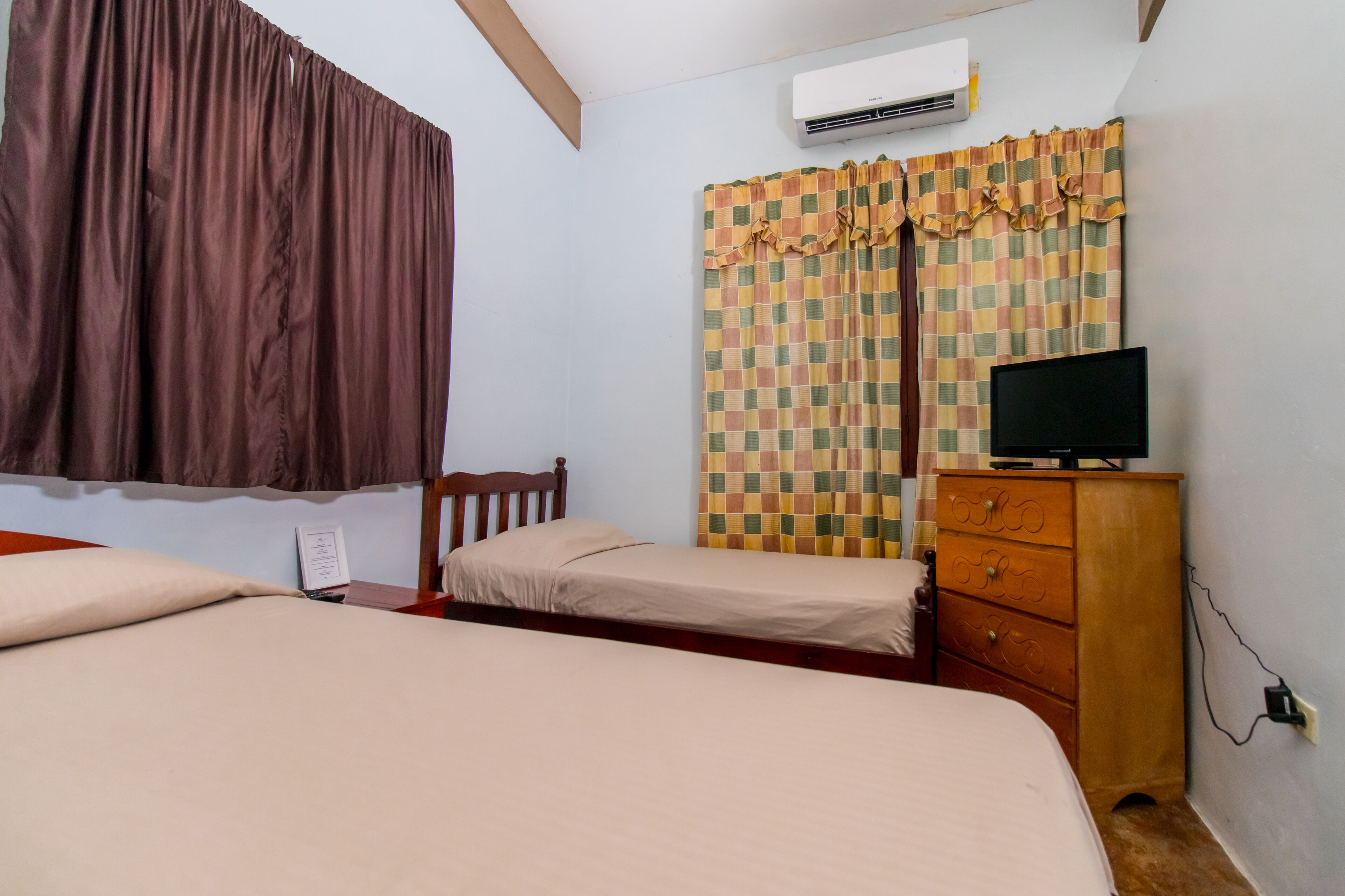 A bedroom with two beds, a wooden dresser, a television, and an air conditioning unit.