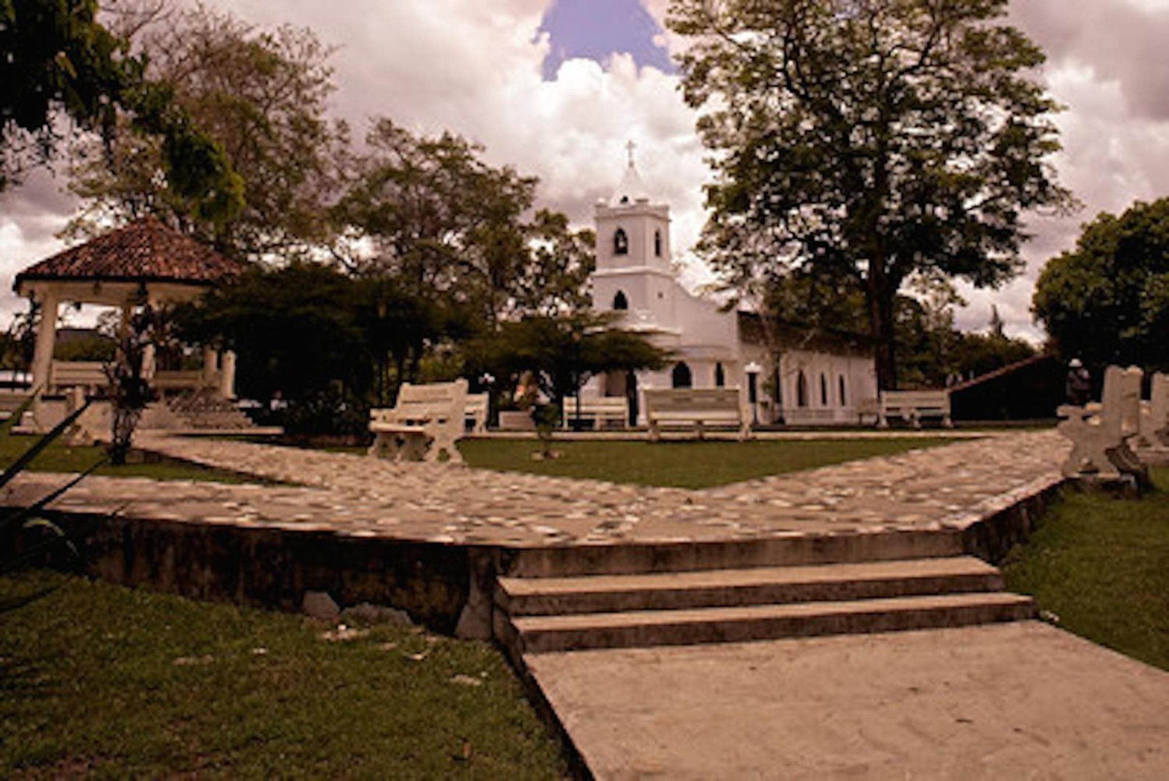 Un edificio histórico con un campanario, rodeado de árboles y un sendero de piedra.
