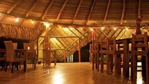 Un espacio interior con techo alto de paja y mobiliario de madera.