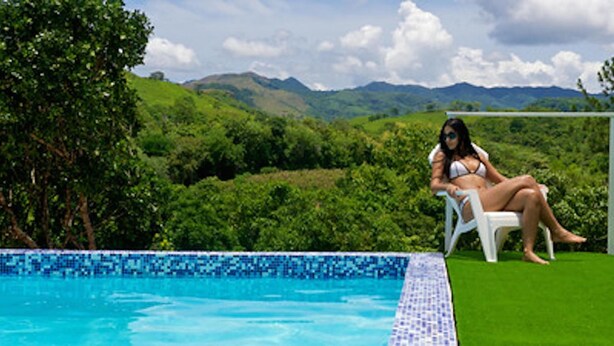 Una piscina con agua cristalina, rodeada de exuberante vegetación y colinas al fondo.