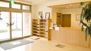 A reception area with a wooden counter, a plant, and a shoe rack. - Yuukaro Showa (Kami)