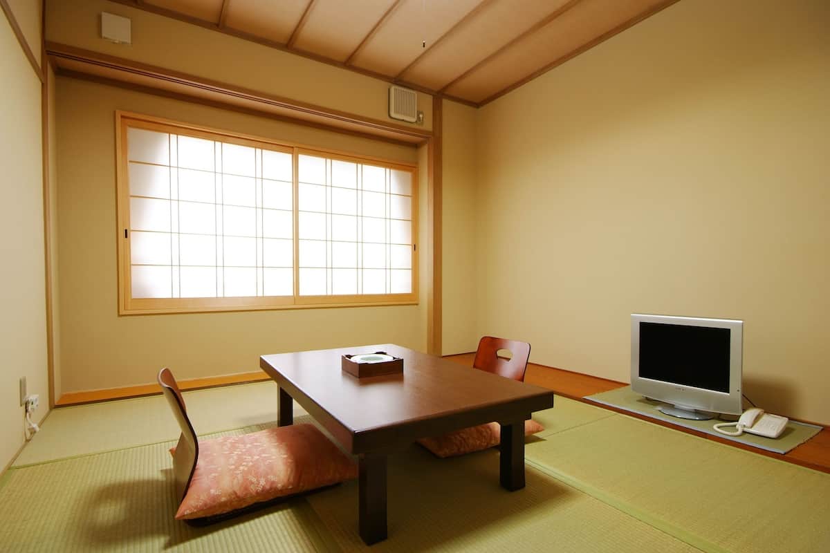 Una habitación japonesa tradicional con suelo de tatami, una mesa baja, un televisor y un teléfono.