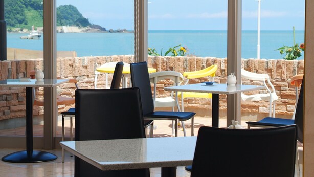 An outdoor seating area with tables and chairs, overlooking a coastal view with a lighthouse and greenery. - Yuukaro Showa (Kami)