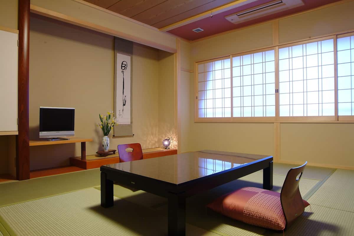 Una habitación japonesa tradicional con suelo de tatami, una mesa baja, un televisor sobre un soporte y una puerta corredera con un diseño de cuadrícula.