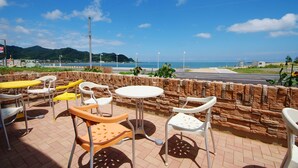 An outdoor seating area with stone walls and metal chairs, overlooking a beach and ocean. - Yuukaro Showa (Kami)